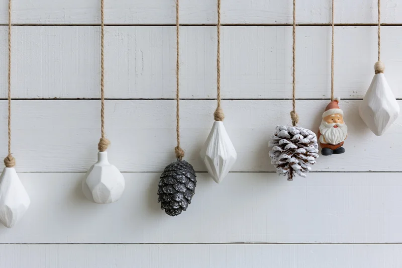 Assorted christmas ornaments hanging from twine strings against a white wooden wall