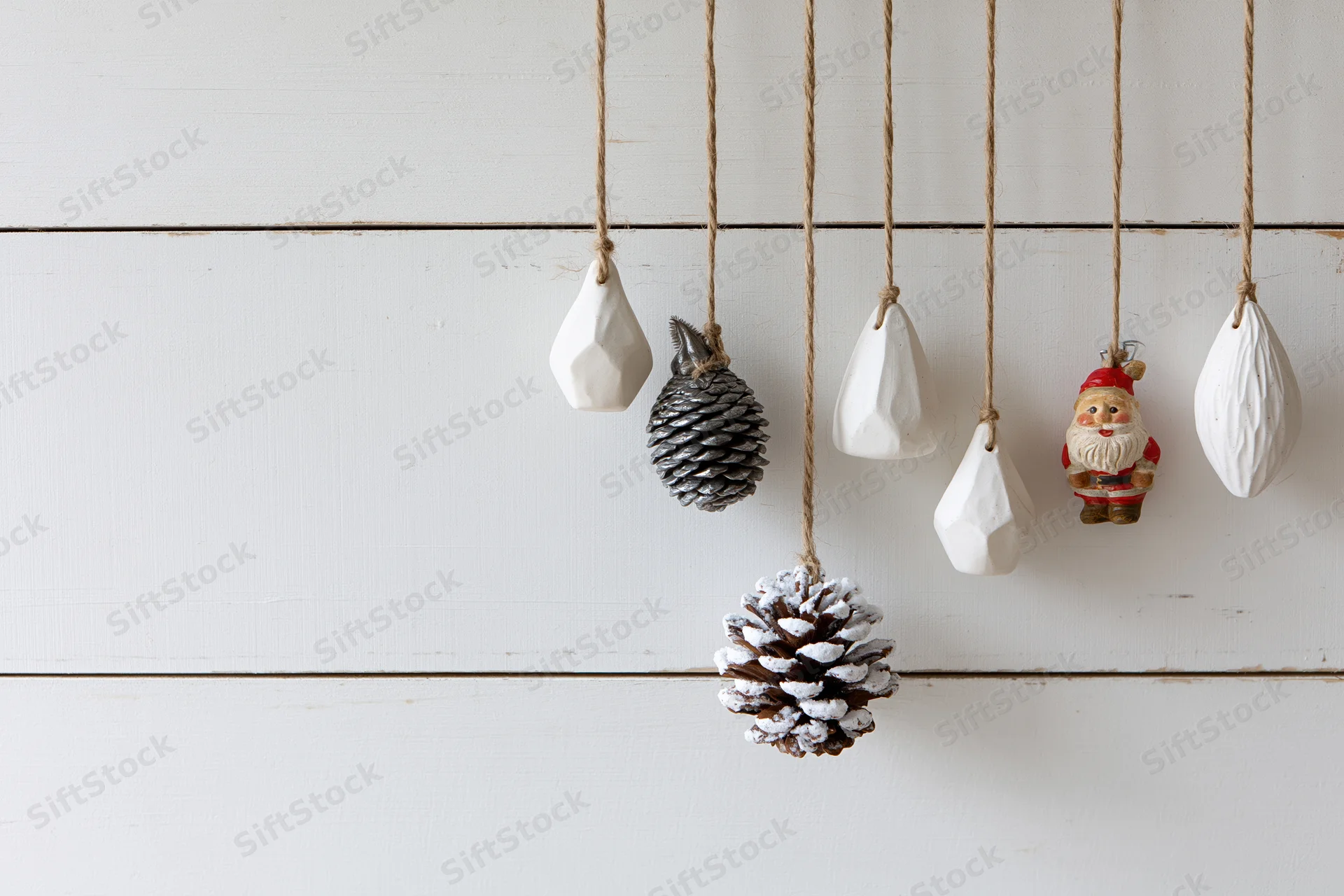 Assorted christmas ornaments hanging from twine strings against a white wooden wall
