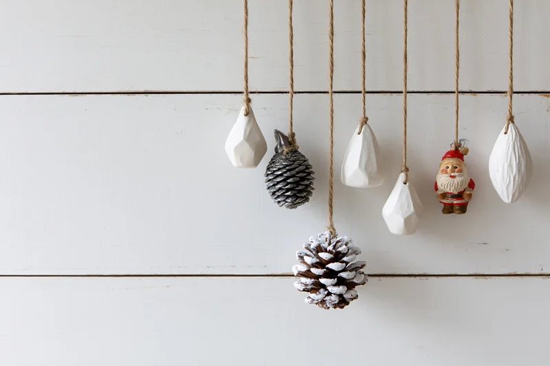 Assorted christmas ornaments hanging from twine strings against a white wooden wall