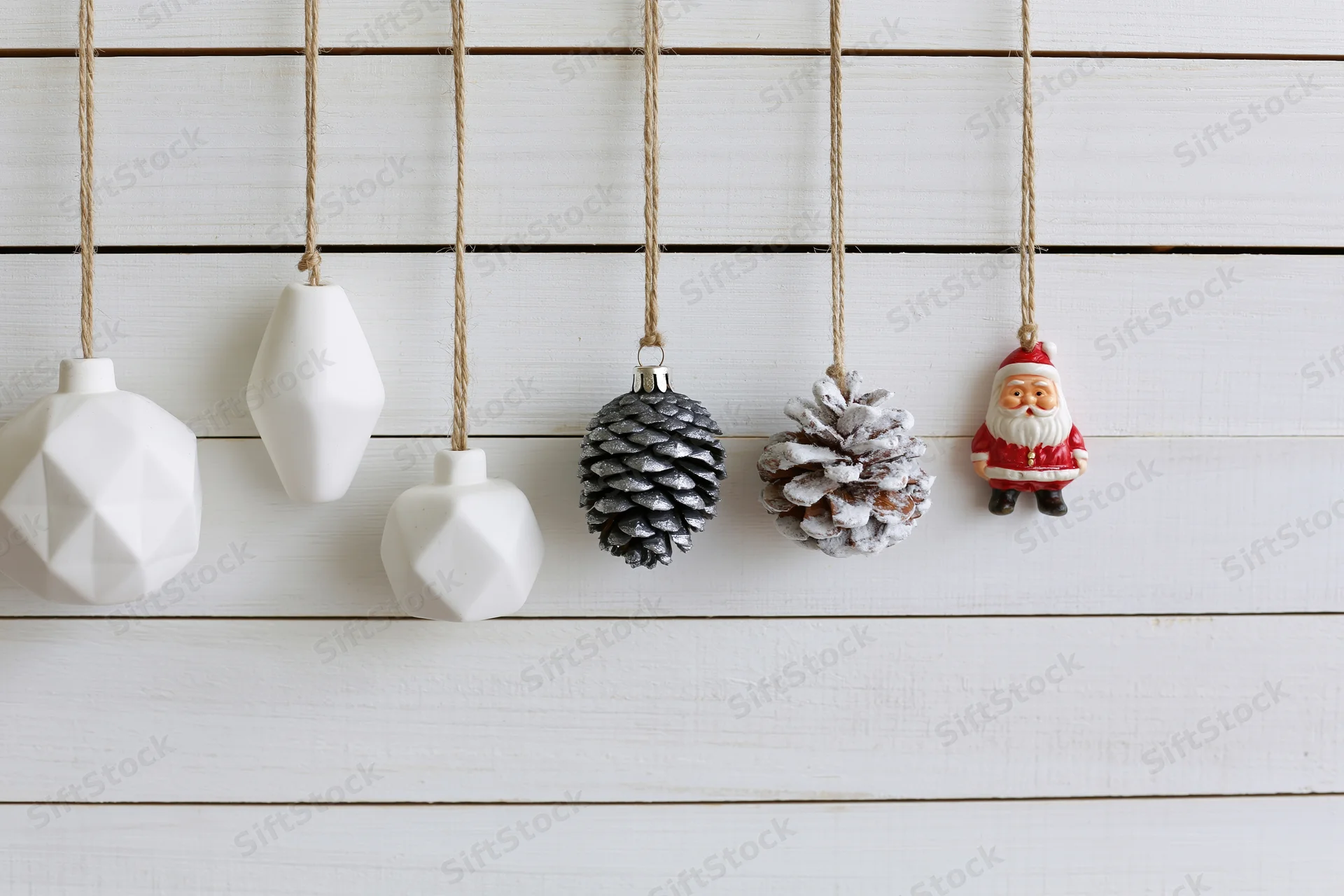Assorted christmas ornaments hanging from twine strings against white wooden wall