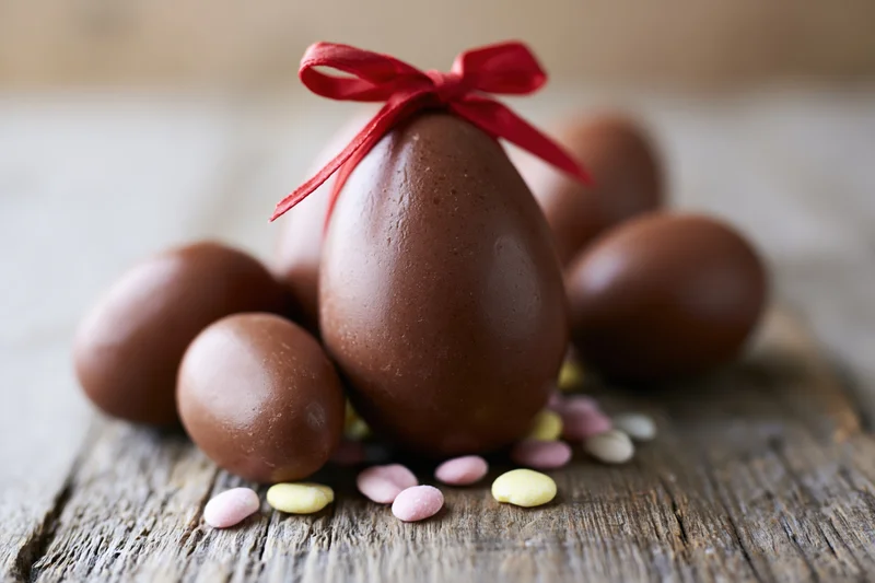Chocolate easter eggs of varying sizes arranged on a rustic wooden surface with colorful sprinkles and a red ribbon bow