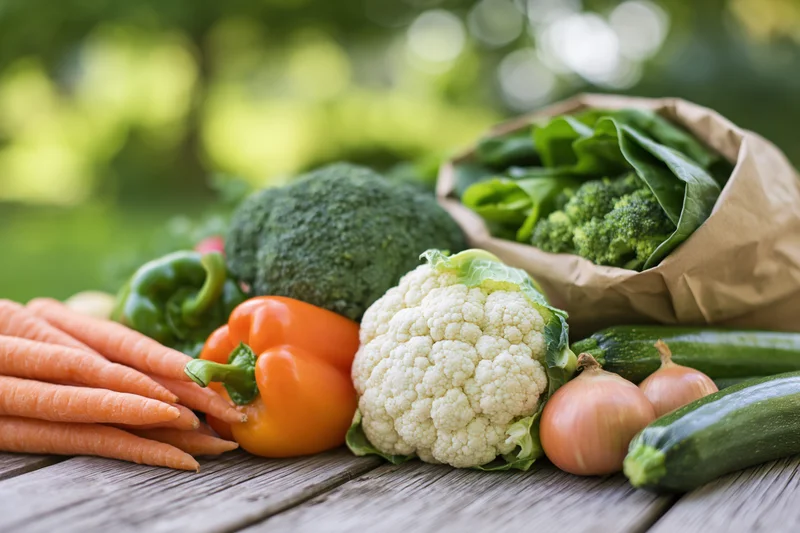 Assorted fresh vegetables arranged on a weathered wooden table outdoors