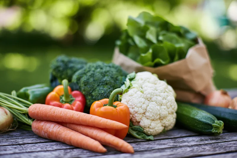 Assorted fresh vegetables arranged on a weathered wooden table outdoors