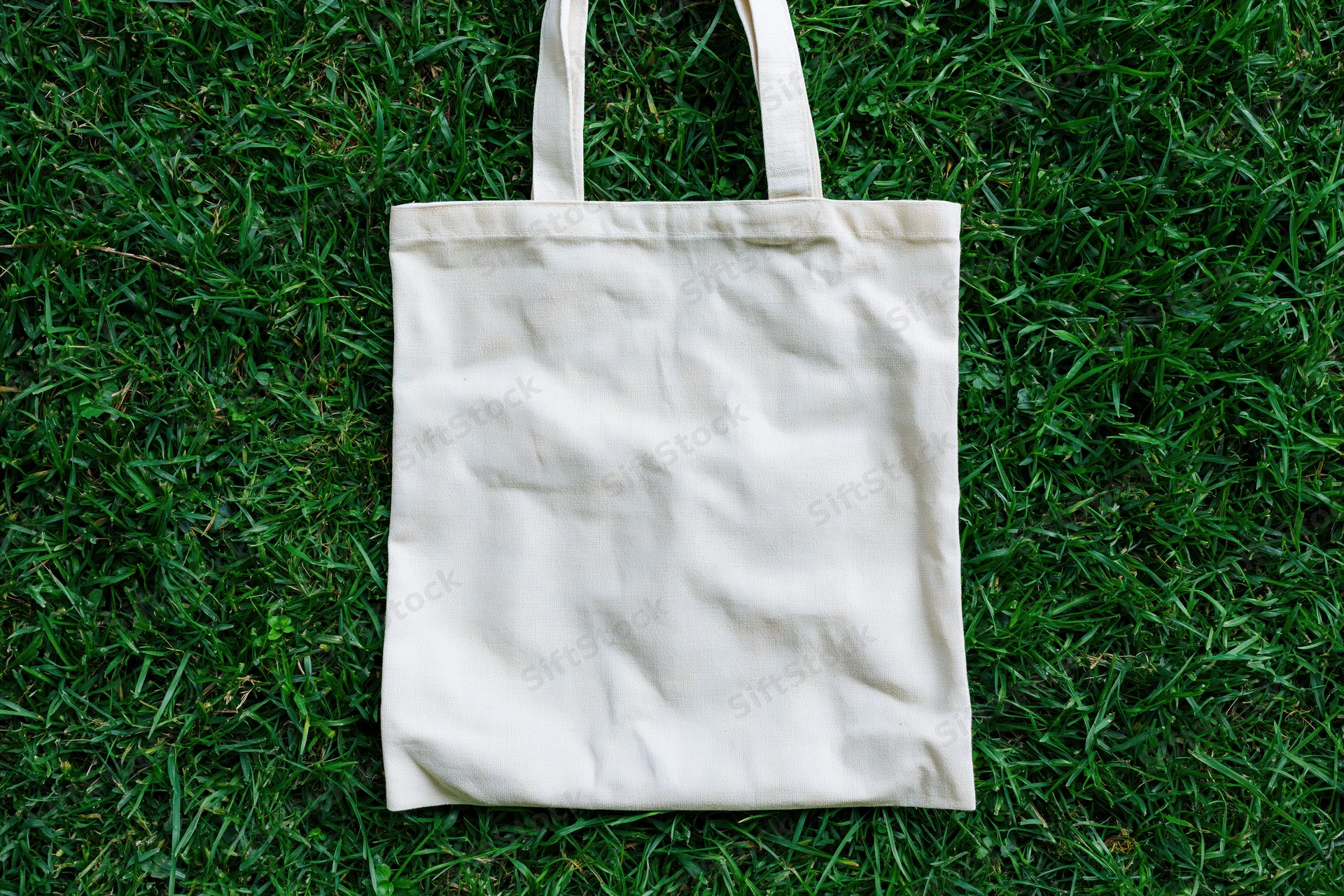 Cream canvas tote bag lying flat on dense green grass