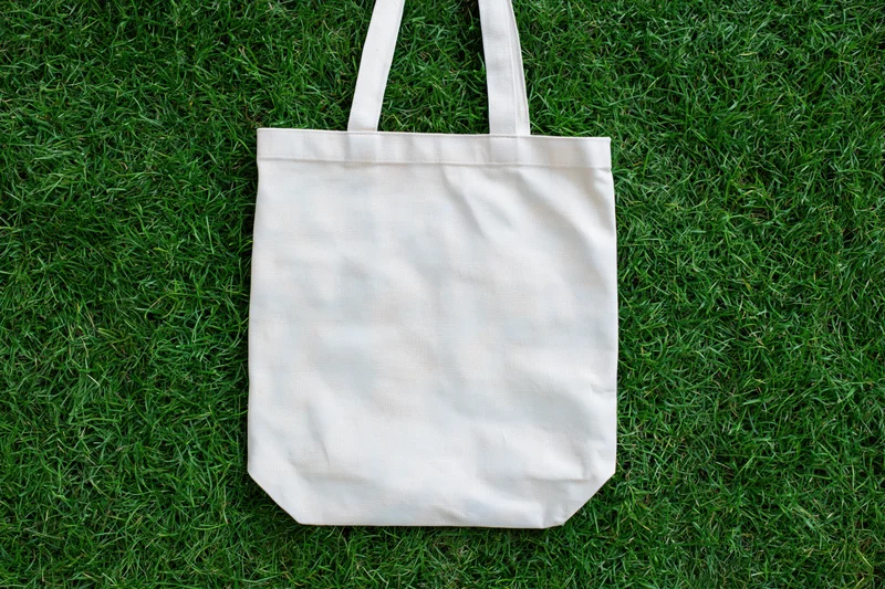 Cream canvas tote bag lying flat on dense green grass