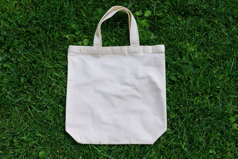 Blank cream canvas tote bag lying flat on dense green grass