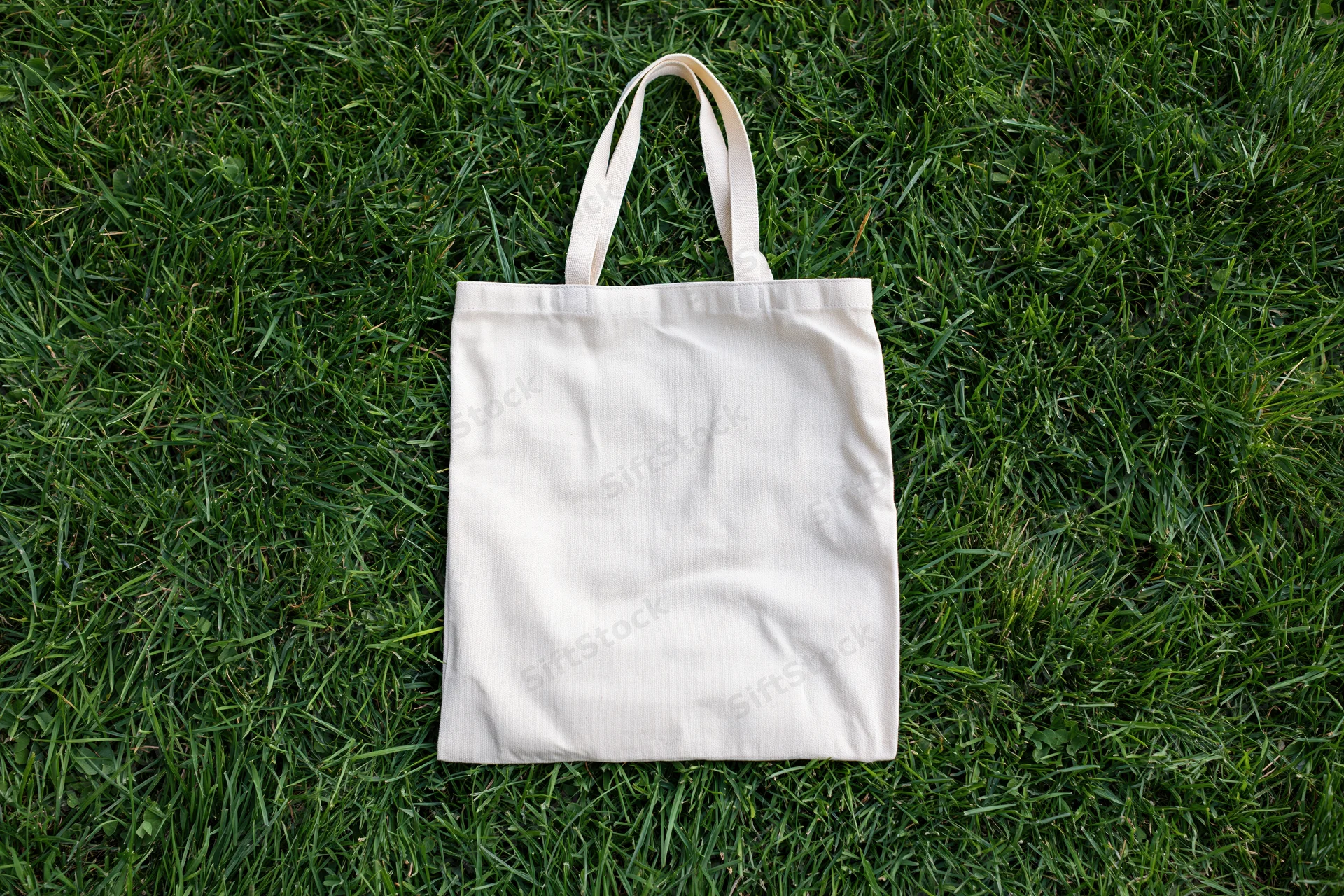 Cream canvas tote bag lying flat on dense green grass