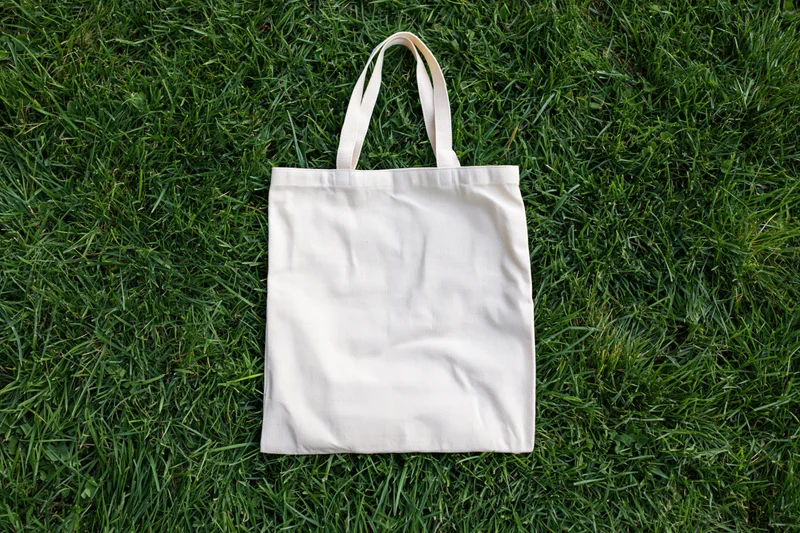 Cream canvas tote bag lying flat on dense green grass