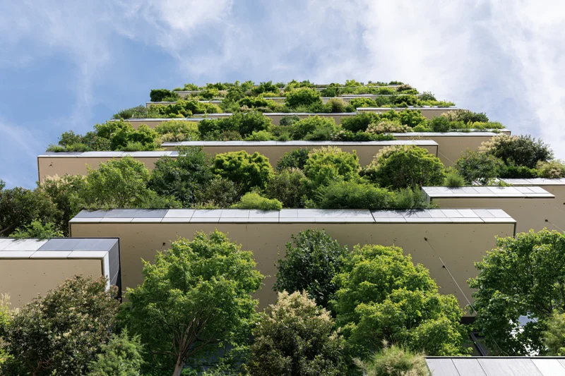 Terraced residential tower facade covered in dense trees and shrubs under a blue sky