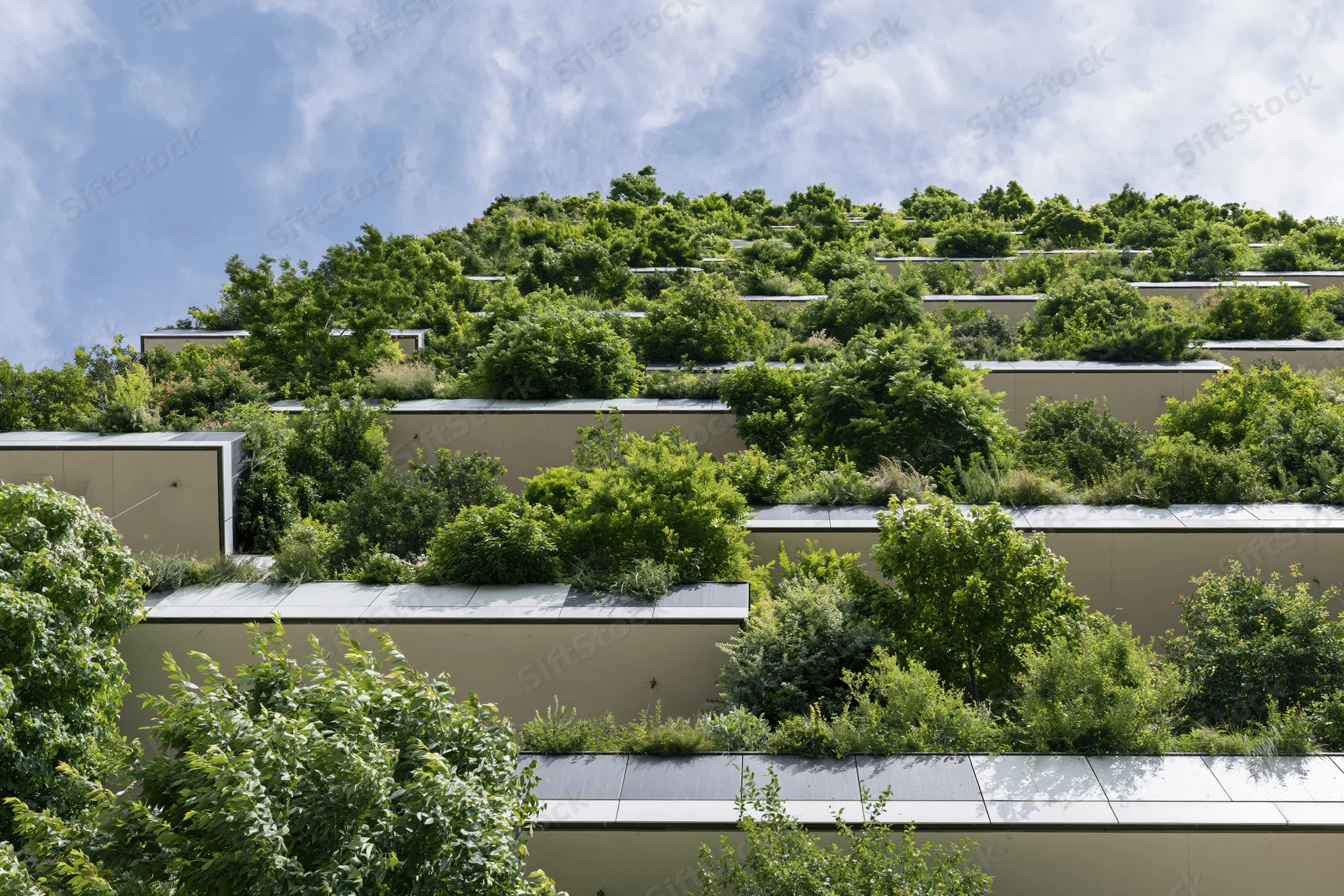Terraced green facade of a residential tower covered in dense trees and shrubs under a partly cloudy sky