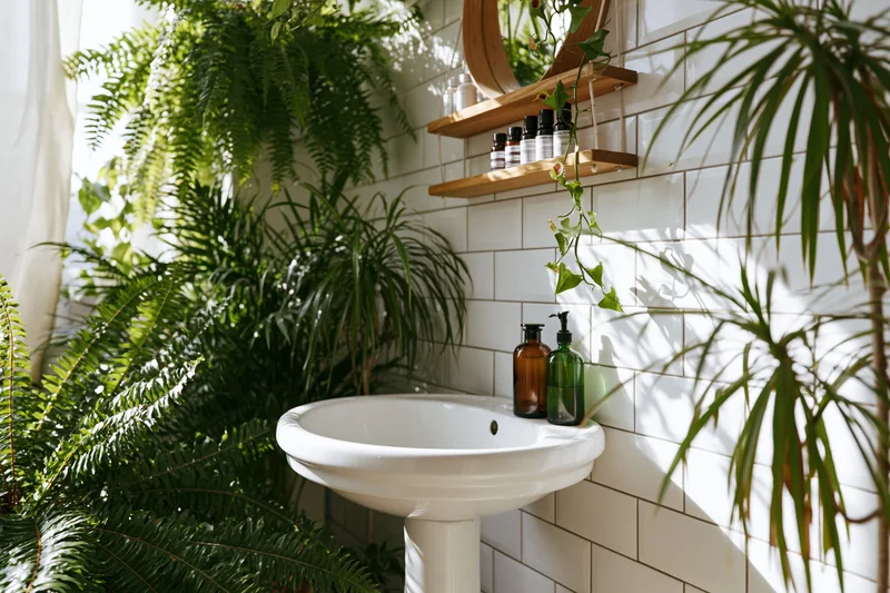 White ceramic pedestal sink surrounded by lush green plants in a tiled bathroom interior