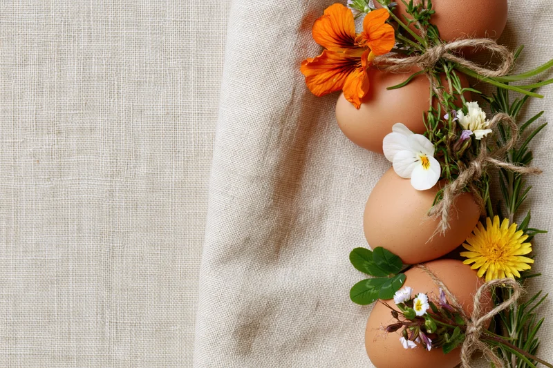 Brown chicken eggs decorated with small wildflowers and fresh herbs arranged on a linen cloth with copyspace