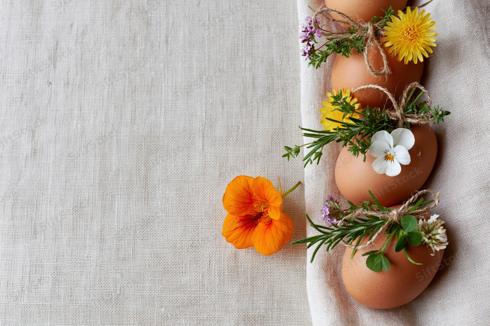 Brown eggs decorated with wildflowers and herbs arranged on a linen cloth