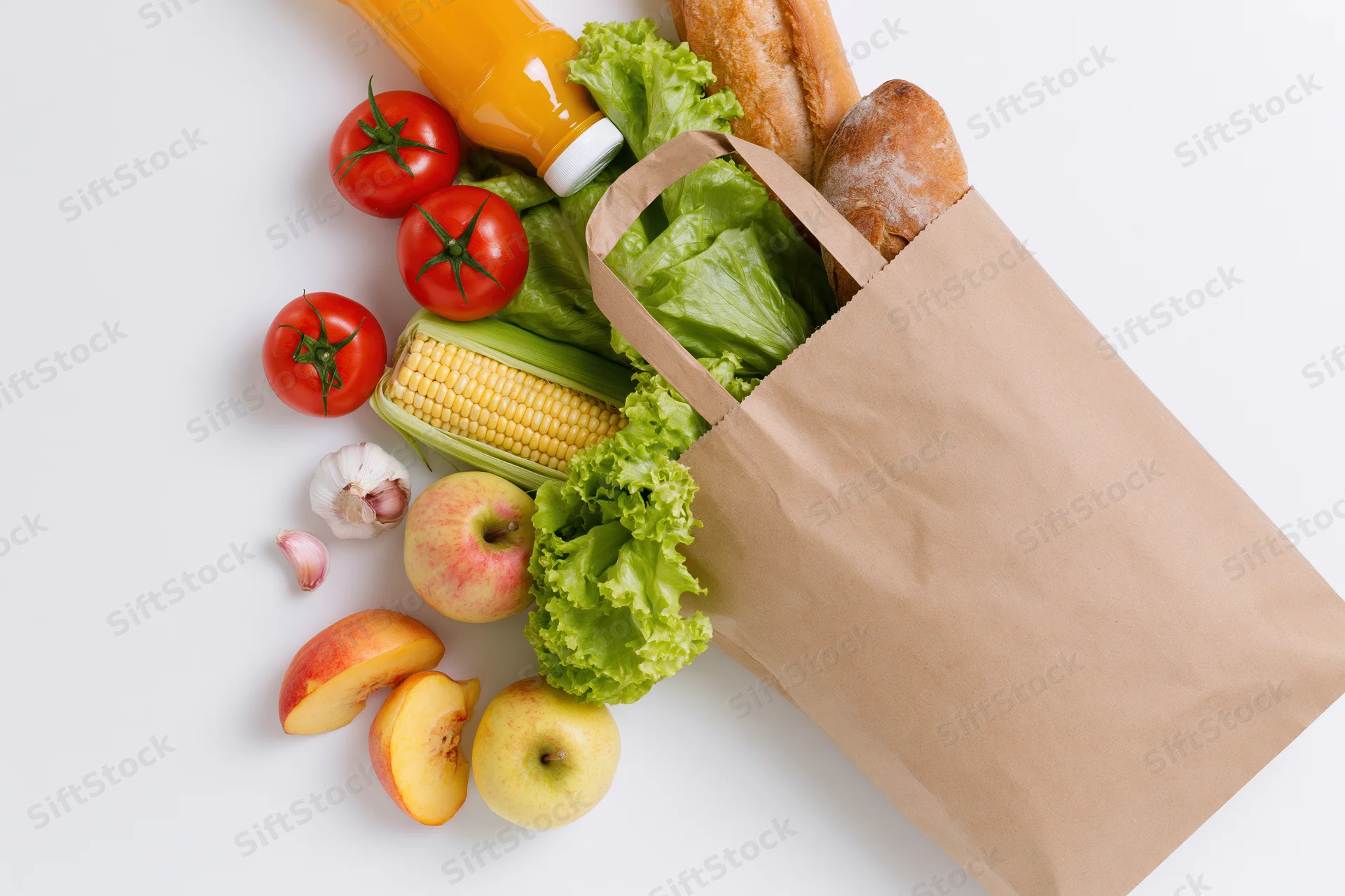 Brown paper grocery bag tipped over spilling fresh vegetables and fruits on white surface