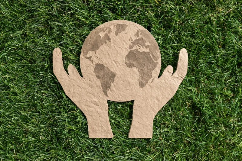 Cardboard cutout of two hands holding a globe on green grass
