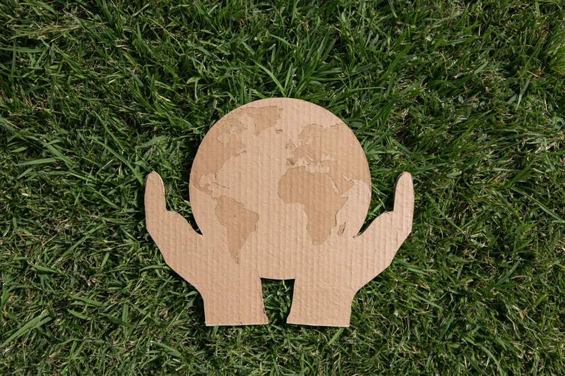 Cardboard cutout of two hands holding a globe on green grass