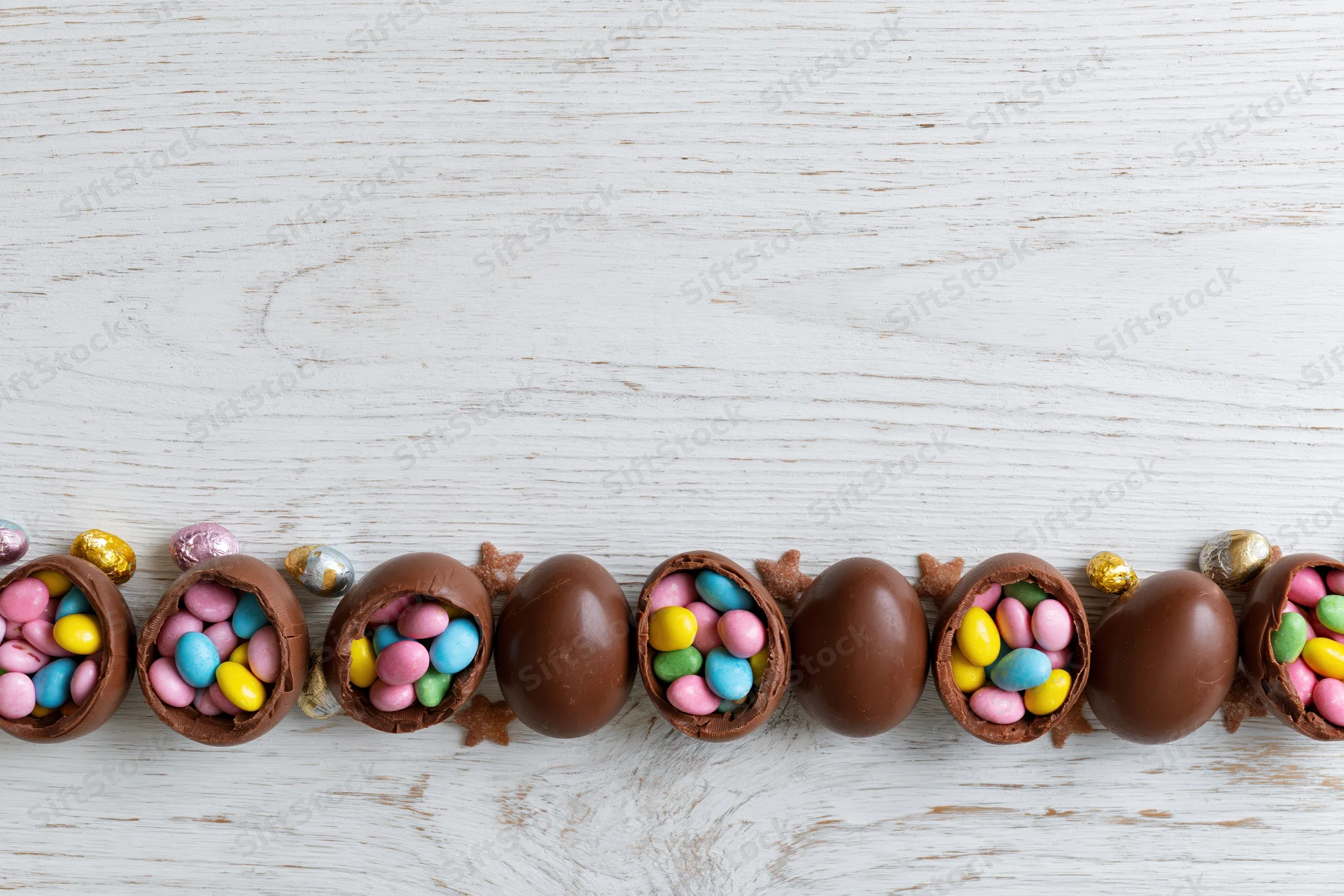 Chocolate easter eggs cracked open and filled with colorful candy arranged in a row on a white wooden surface