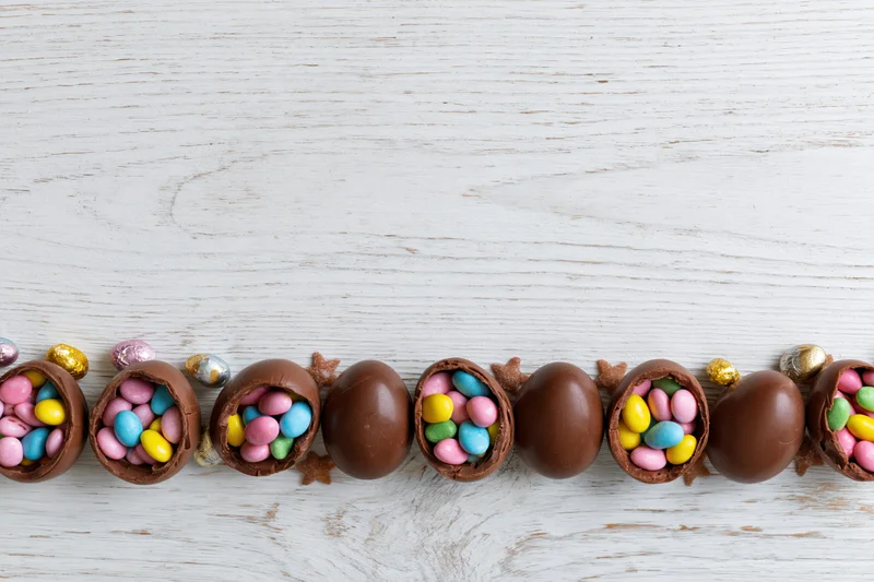 Chocolate easter eggs cracked open and filled with colorful candy arranged in a row on a white wooden surface