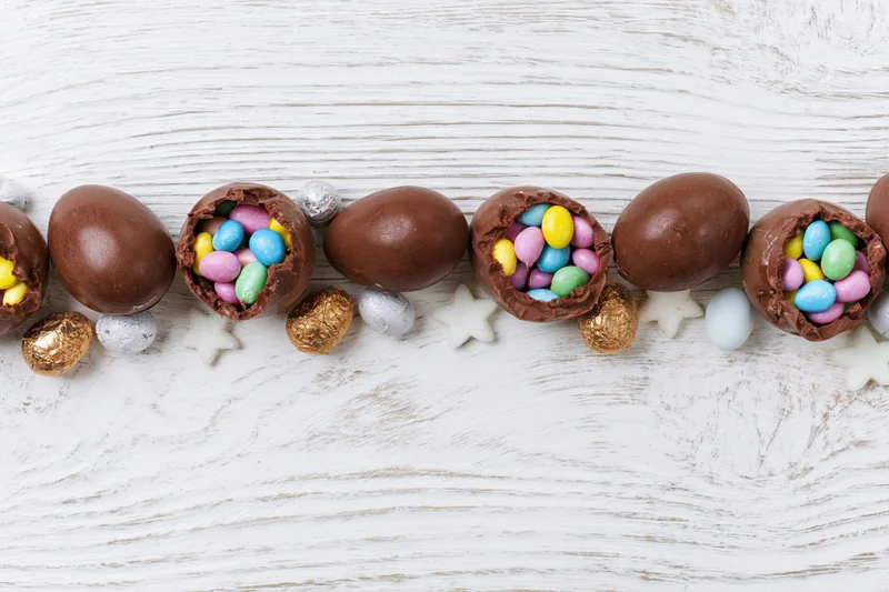 Chocolate easter eggs cracked open and filled with colorful candy arranged in a row on a white wooden surface