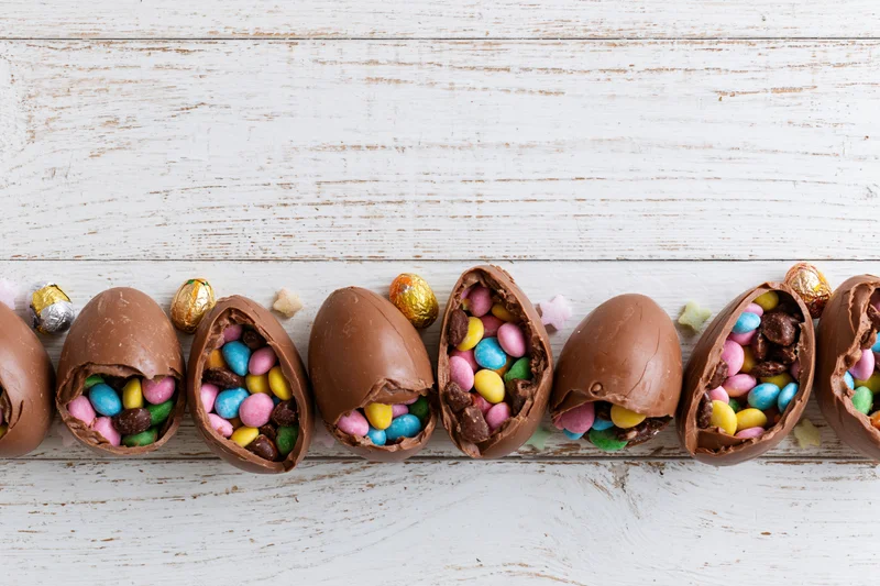 Cracked chocolate easter eggs filled with colorful candy arranged in a row on a white wooden surface
