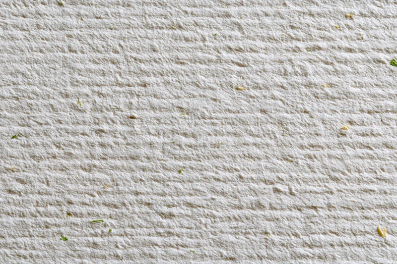 Close-up flat lay of off-white recycled paper with visible fibers and green plant fragments scattered across its textured surface