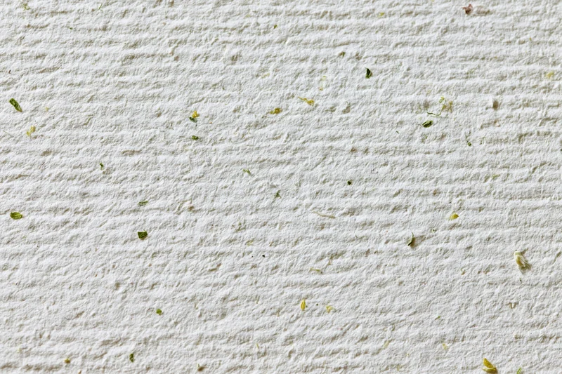 Close-up flat lay of off-white recycled paper with scattered green plant fragments on textured surface