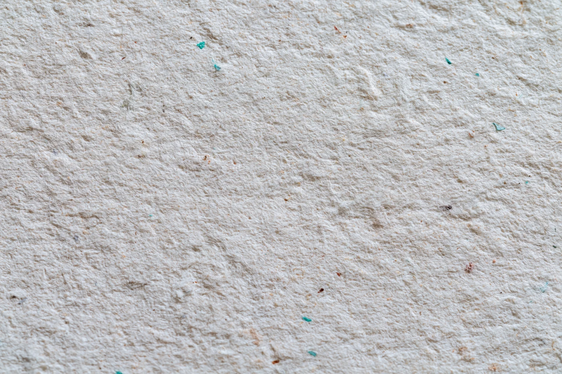 Close-up flat lay of a textured recycled cardboard sheet with colored flecks scattered across its surface