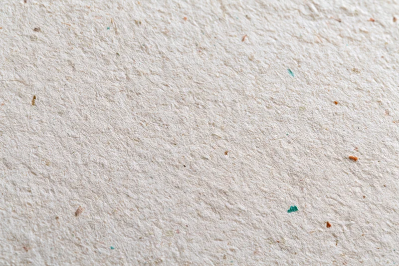 Close-up flat lay of textured recycled paper surface with colored fiber specks