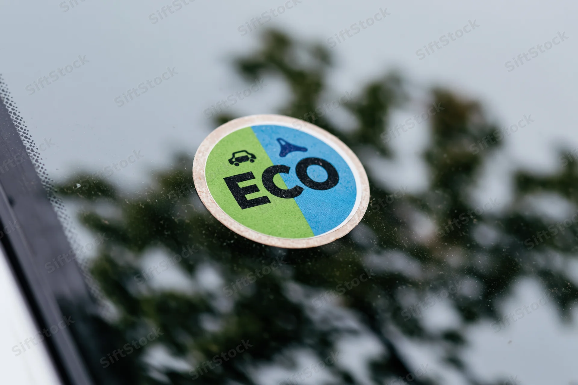 Close-up of a spanish dgt eco environmental sticker affixed to a car window with trees reflected in the glass