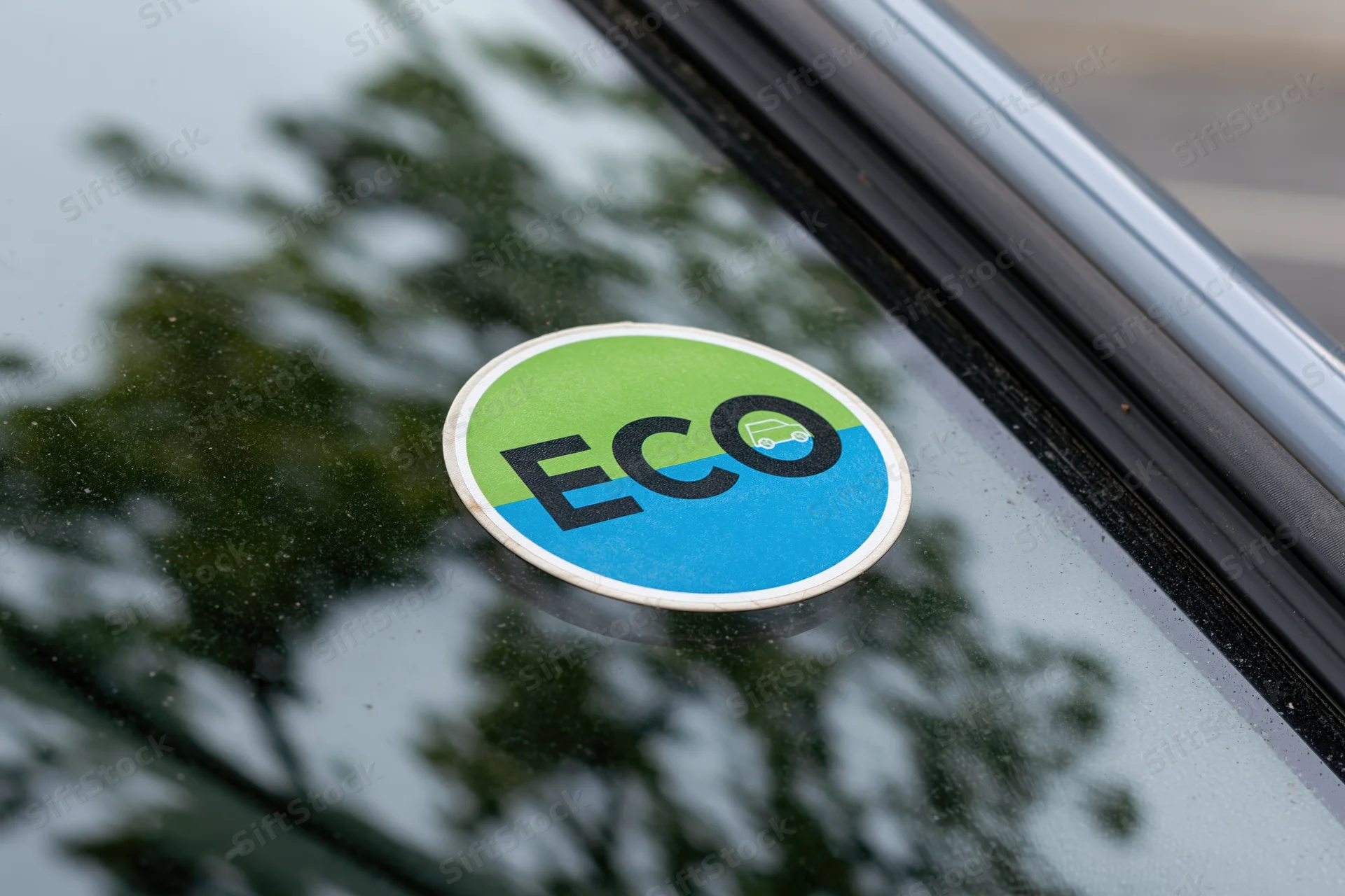 Circular eco sticker affixed to car window reflecting trees outdoors