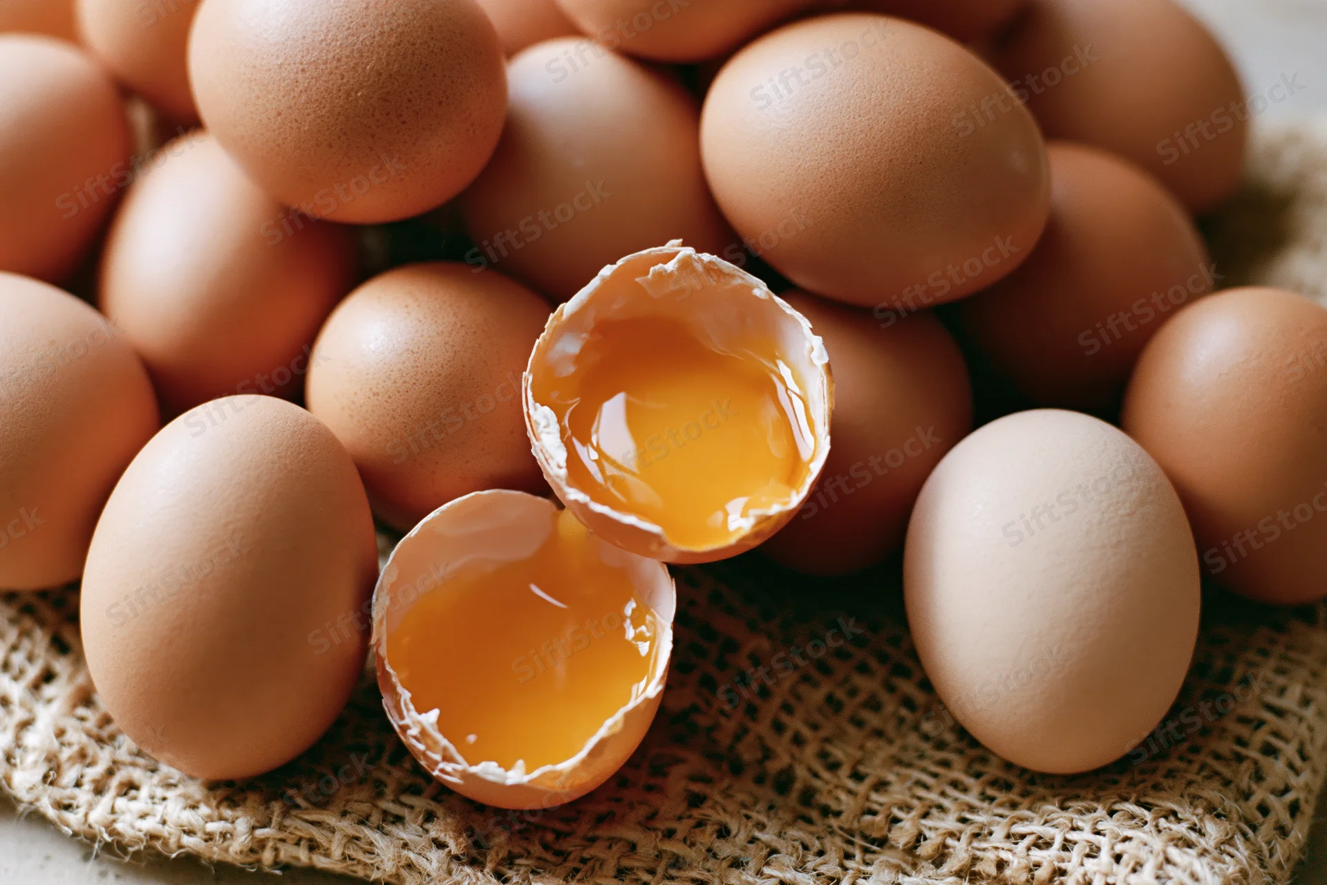 Cracked brown chicken egg split in two halves on burlap surface surrounded by whole eggs
