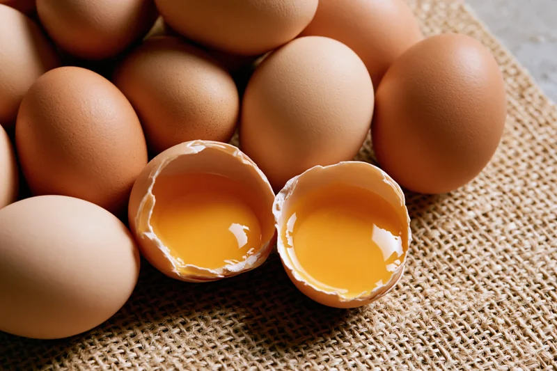 Cracked brown chicken egg split in two halves on burlap surface with whole eggs around