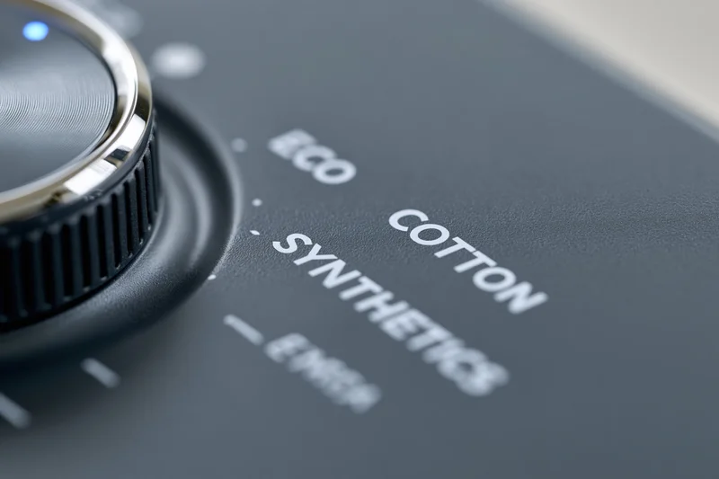 Close-up of a modern washing machine control panel with a rotating dial and fabric cycle labels on a dark grey surface