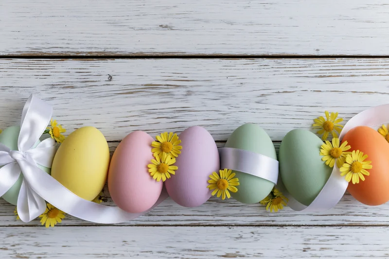 Pastel easter eggs arranged in a row on a white wooden surface with ribbons and small yellow flowers