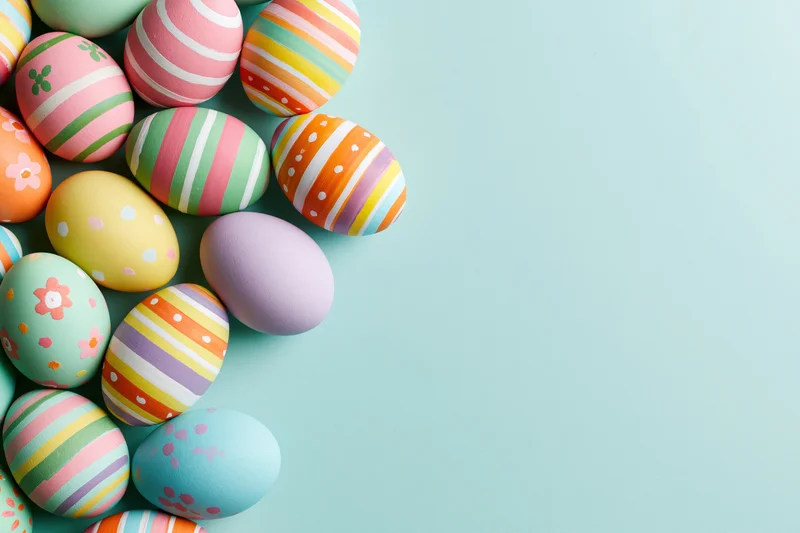 Colorful hand-painted easter eggs arranged in a loose cluster on a light blue background with copyspace