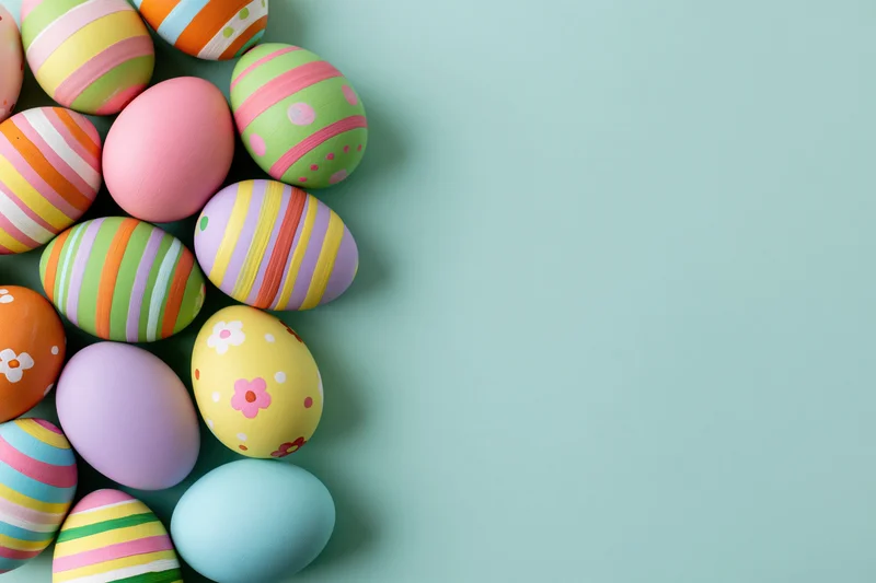 Colorful hand-painted easter eggs arranged in a loose cluster on a teal background with copyspace