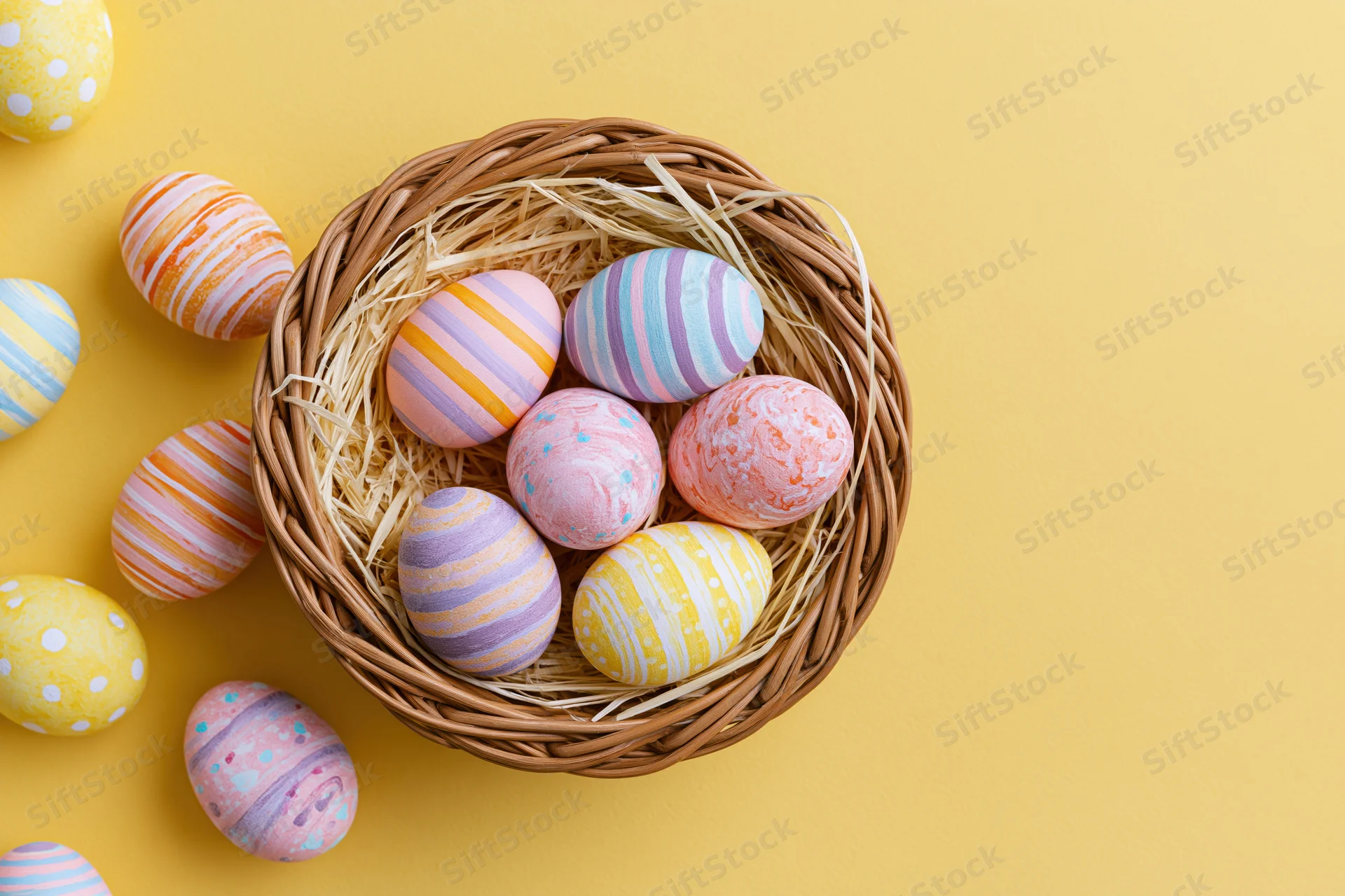 Colorful hand-painted easter eggs arranged in a wicker basket with straw on a yellow background