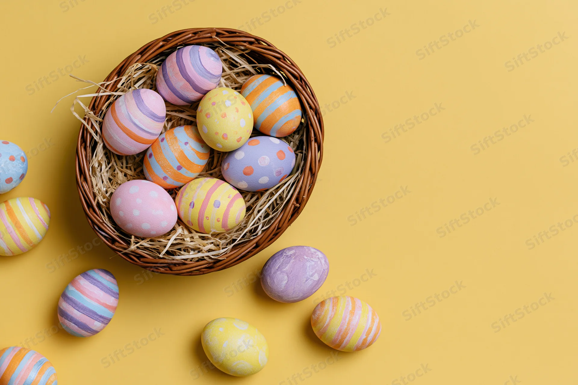 Colorful hand-painted easter eggs arranged in a wicker basket with straw on a yellow background