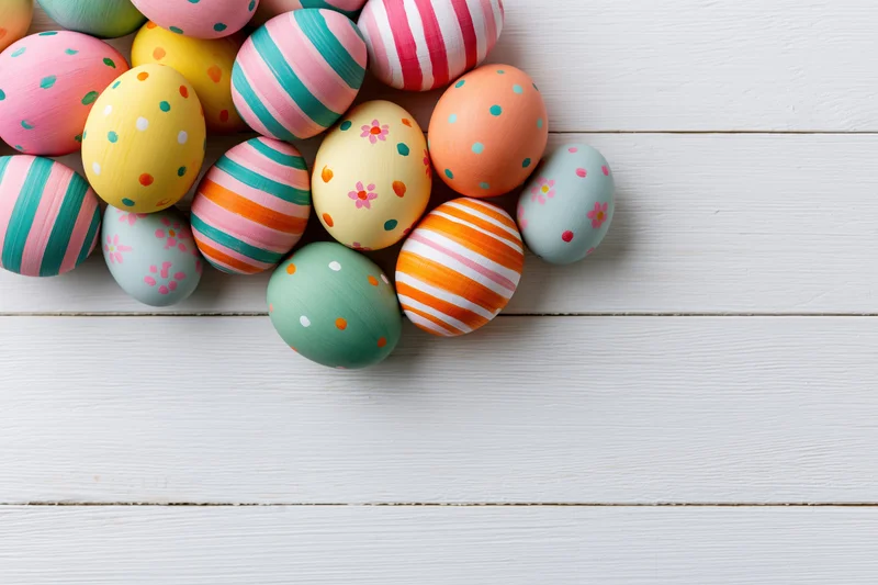 Colorful hand-painted easter eggs clustered along the left edge of a white wooden surface