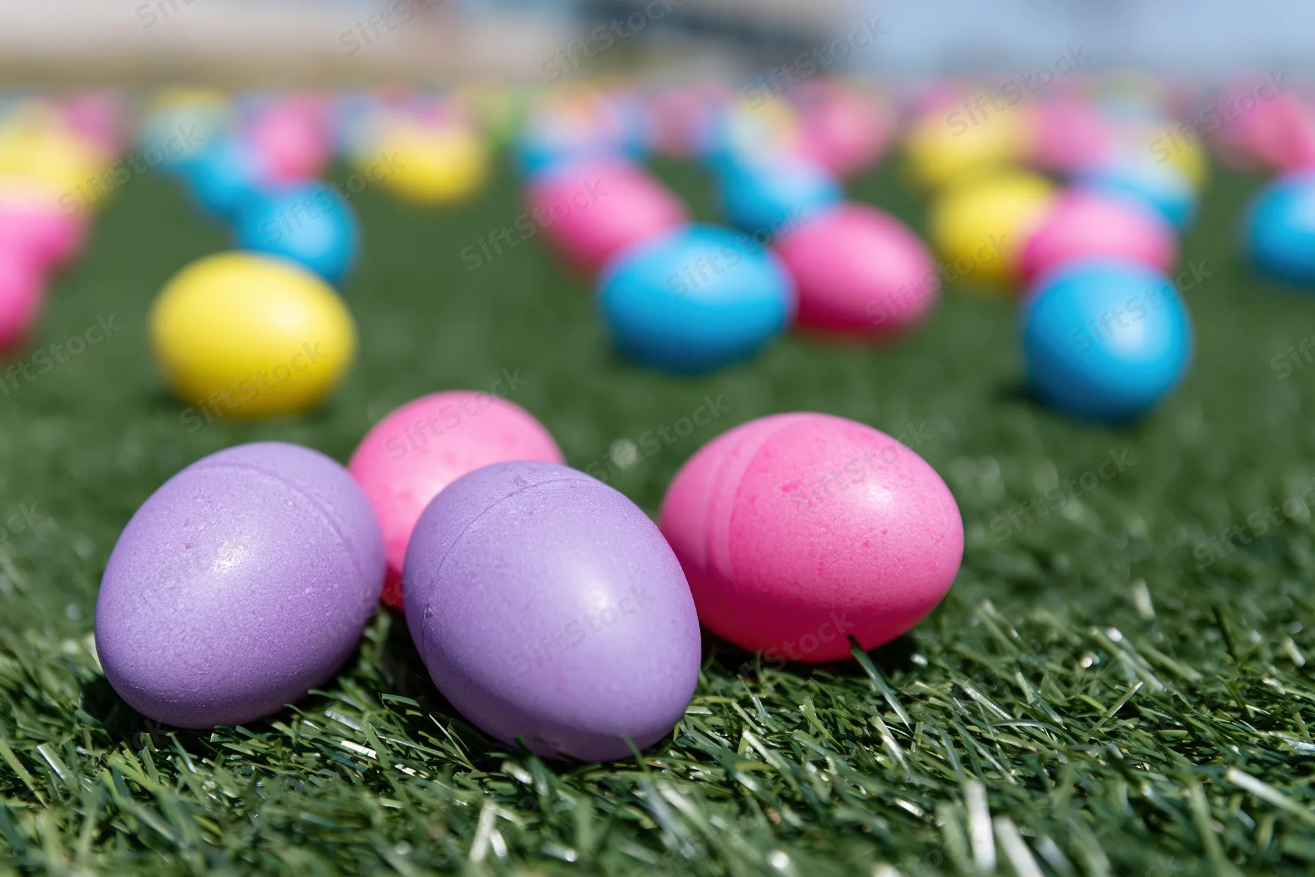 Colorful plastic easter eggs scattered across green artificial grass lawn