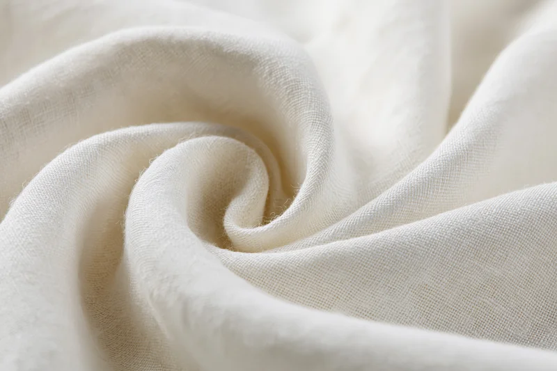 Cream-white linen fabric draped in soft flowing folds forming a swirl