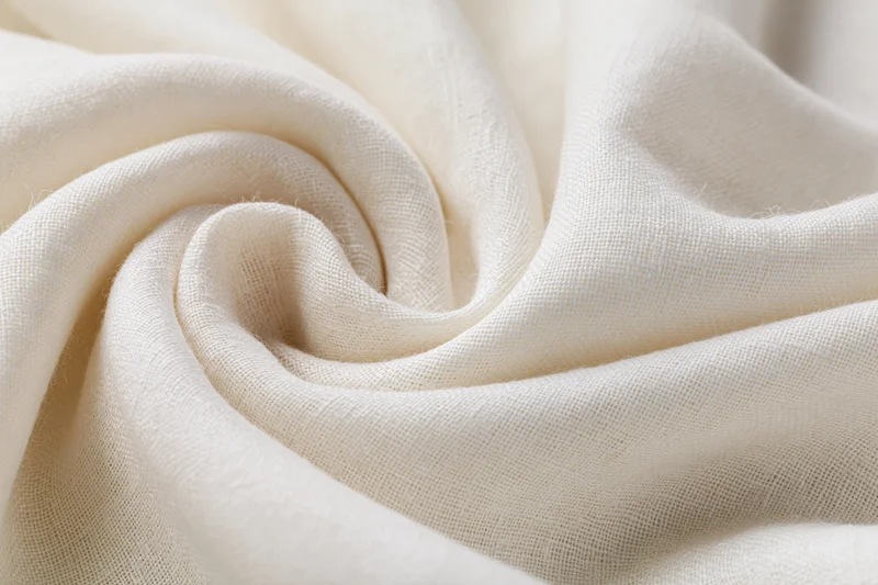 Cream-white linen fabric draped in soft flowing folds with swirling texture