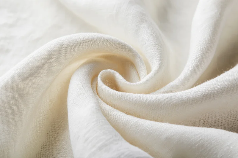 Cream-white linen fabric draped in soft flowing folds forming a swirl