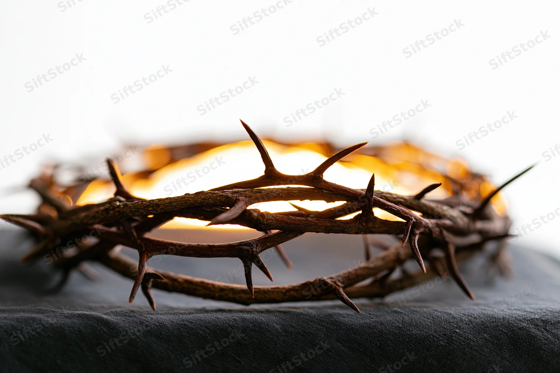 Crown of thorns resting on dark cloth surface in close-up view with glowing light behind