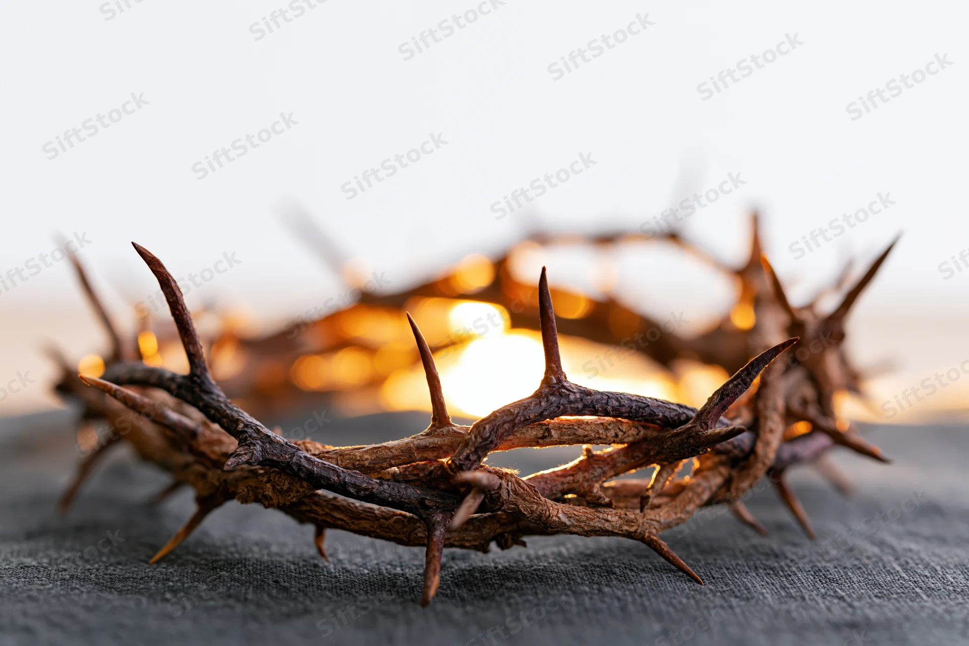 Crown of thorns resting on dark cloth surface close-up with warm bokeh background