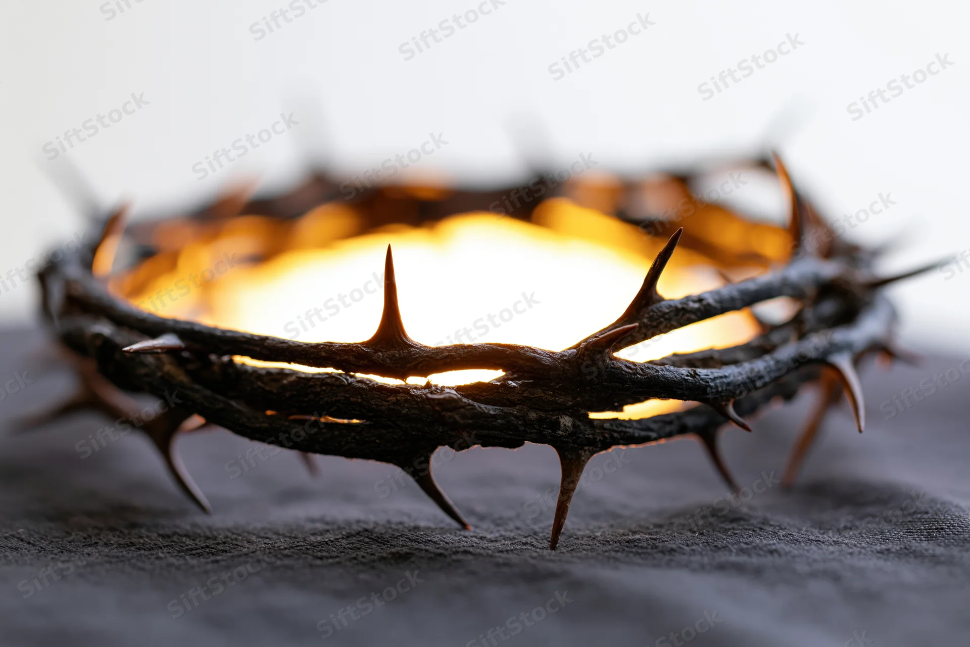 Crown of thorns resting on dark cloth surface in close-up view with glowing light behind