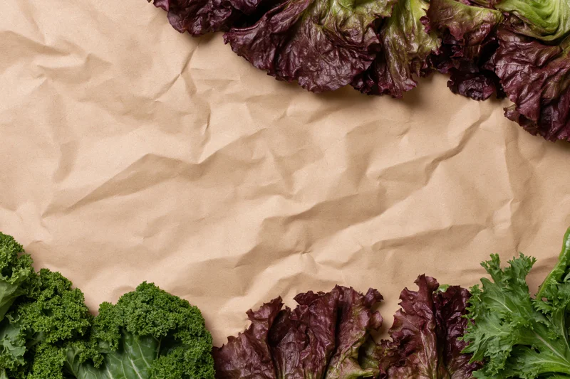 Fresh leafy vegetables arranged along the edges of crumpled kraft paper background