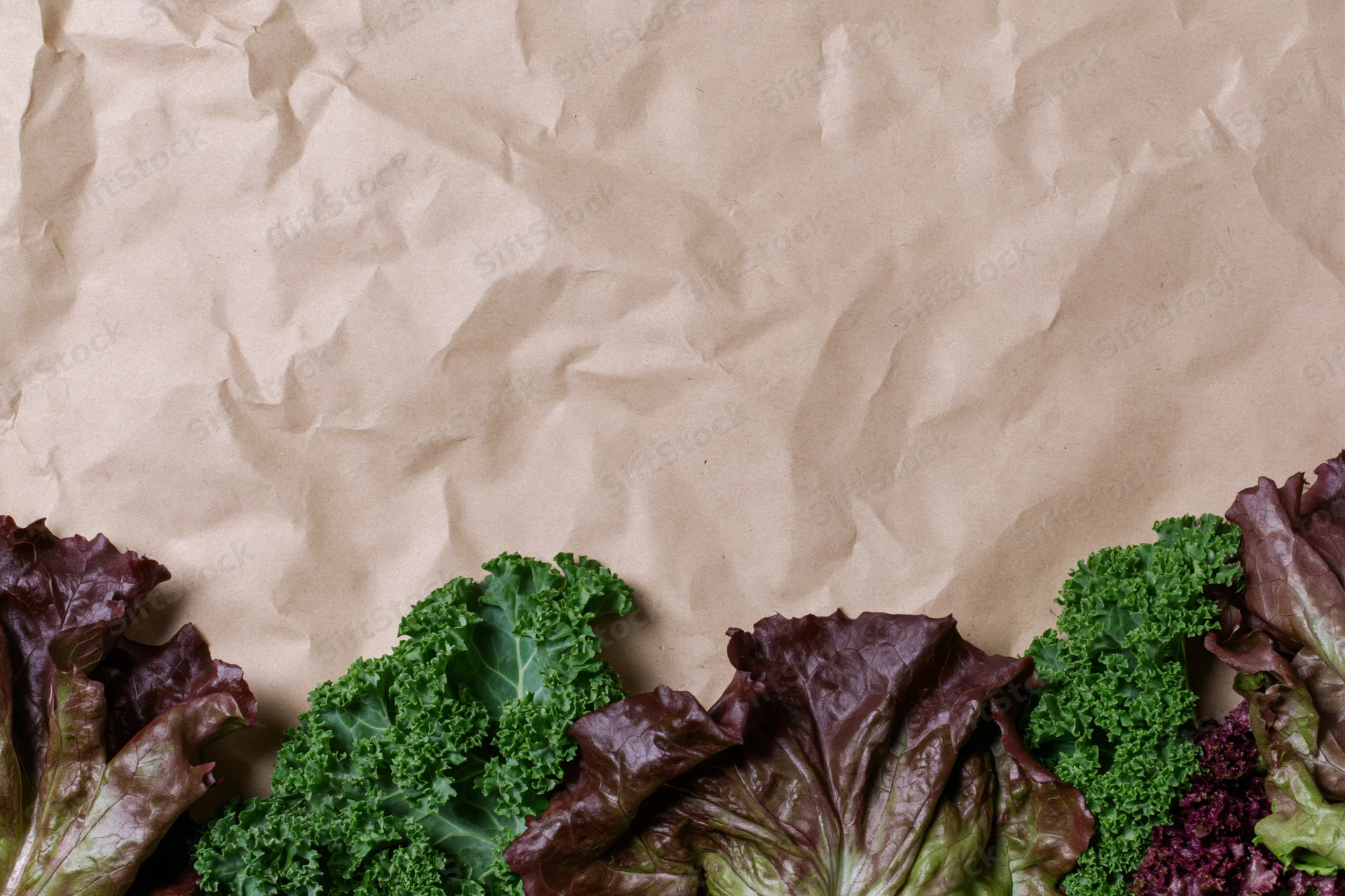Fresh leafy vegetables arranged along the bottom edge of crumpled kraft paper background