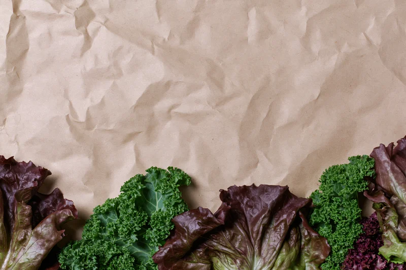 Fresh leafy vegetables arranged along the bottom edge of crumpled kraft paper background