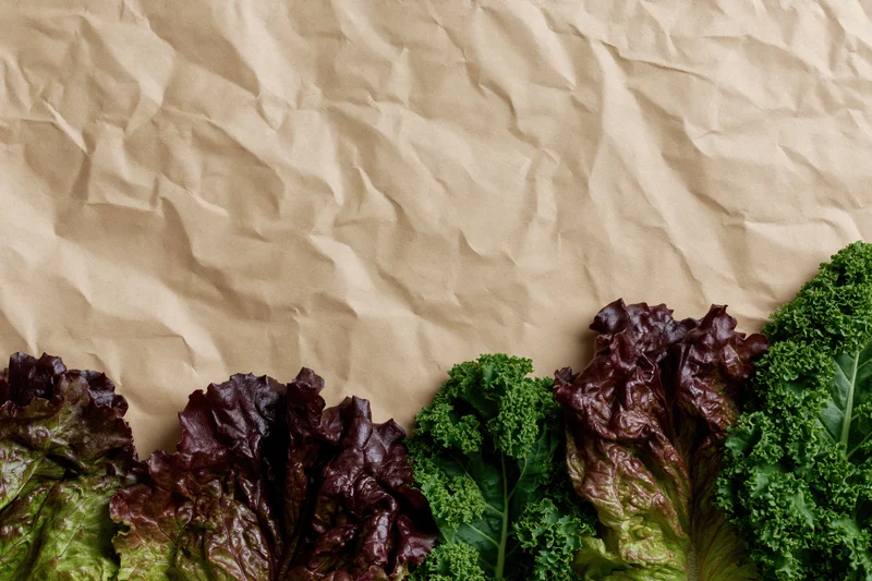 Fresh leafy vegetables arranged along the bottom edge of crumpled kraft paper background